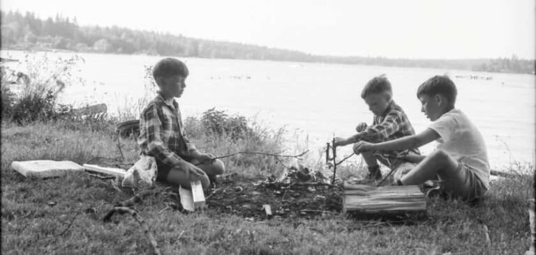 Drie jongens zitten in de jaren vijftig rond kampvuur aan het water
