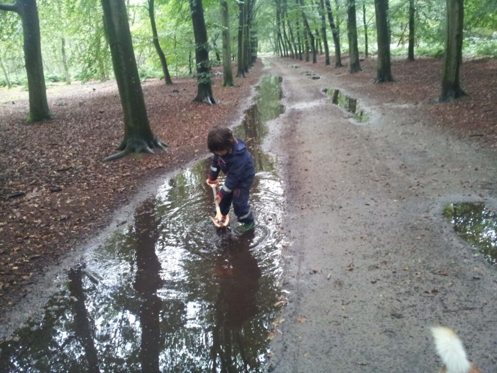 Zoontje speelt in de plassen na de regen.