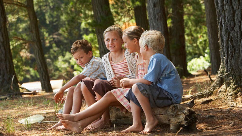Kinderen zitten in de zomer op een boomstam en lopen op blote voeten in het bos.