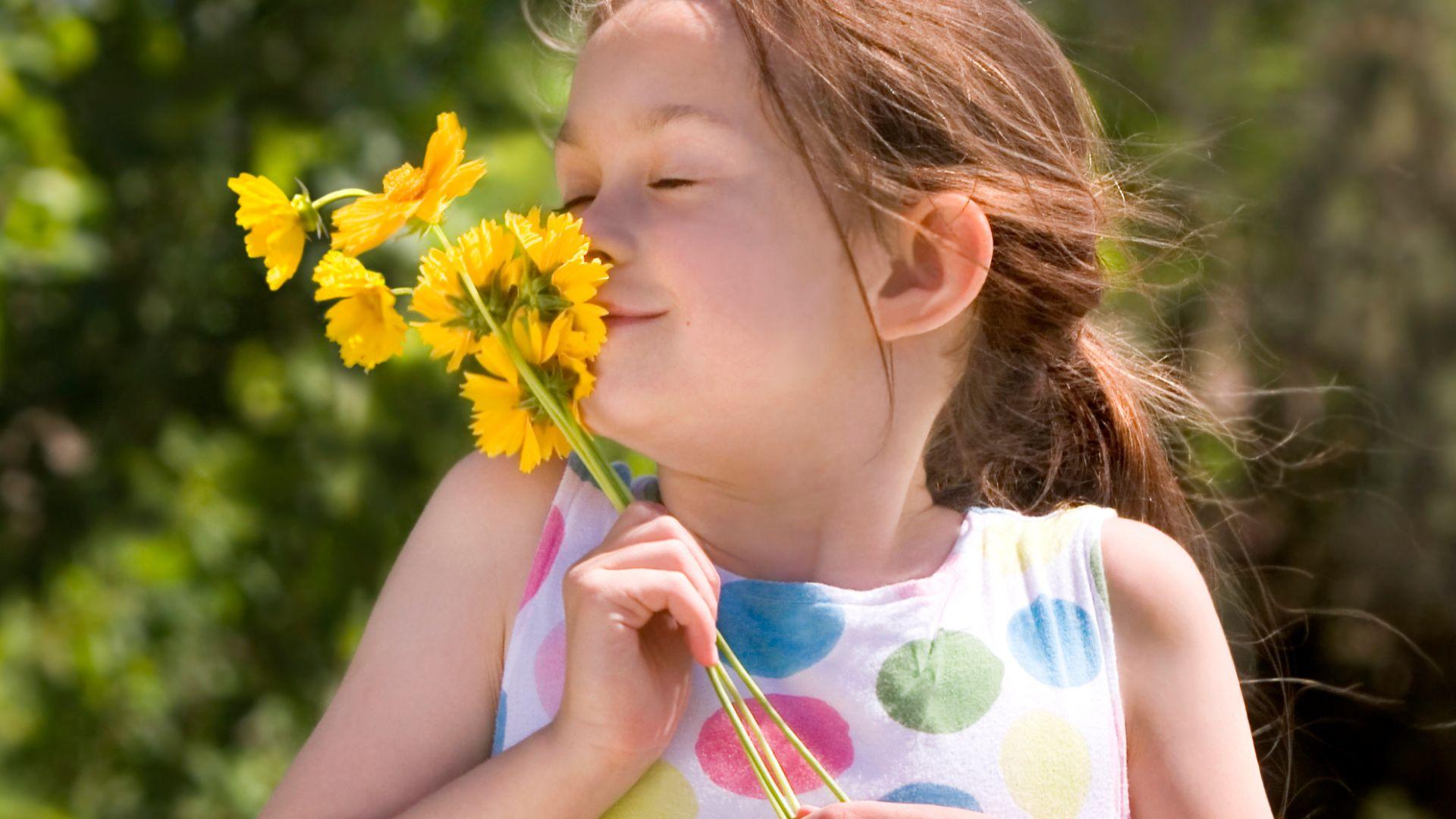 Een meisje ruikte aan een gele bloem en houdt haar ogen dicht.