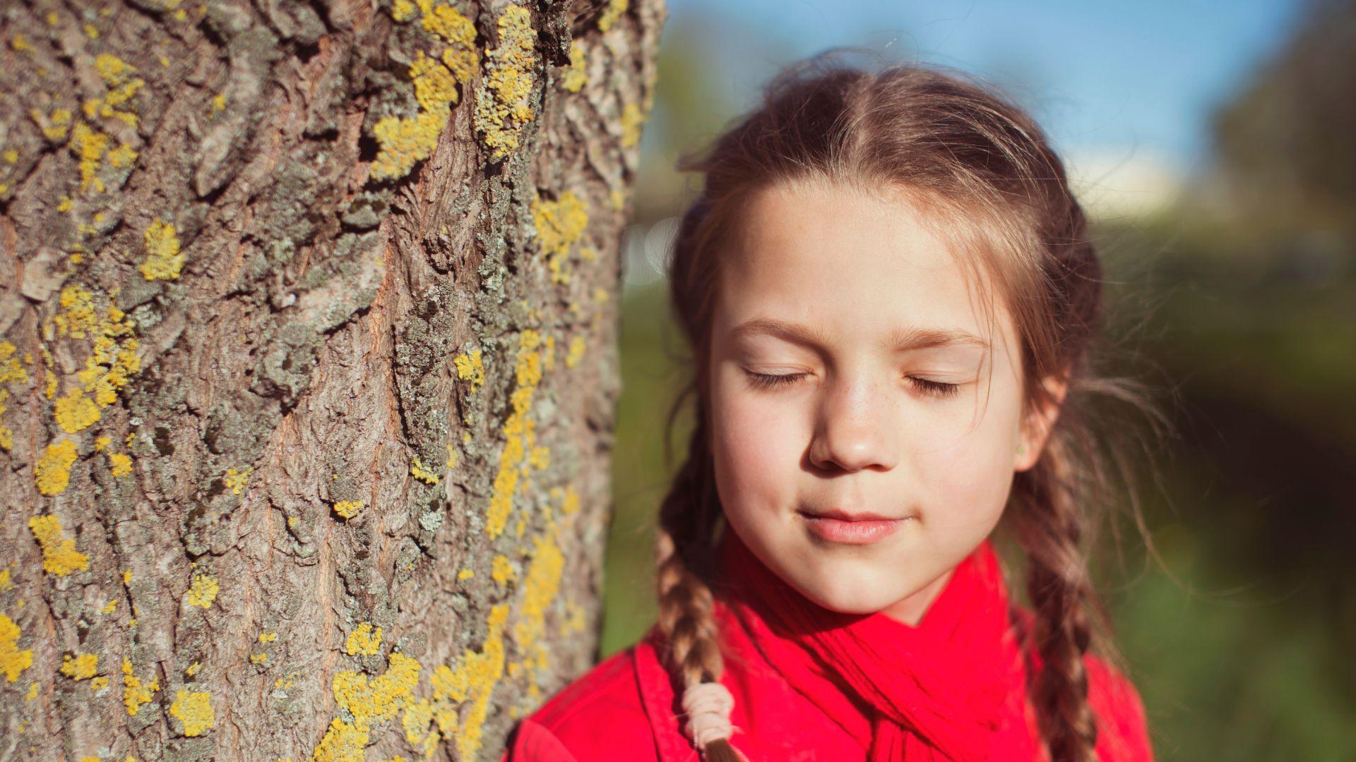 Een meisje met vlechten houdt haar ogen dicht bij een boomstam met mos.